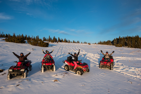 Group of people sitting with hands up on four-wheelers ATV bikes in the the mountains in winter eveningの写真素材