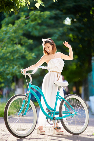 A blue retro bicycle near a beautiful girl in summer sunlight on a blurred background of city greenery.の写真素材