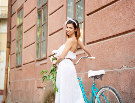 Low angle horizontal shot of a beautiful happy woman walking with her bicycle on the city street smiling to the camera over her shoulder copyspace beauty positivity weekend travel tourism.の写真素材