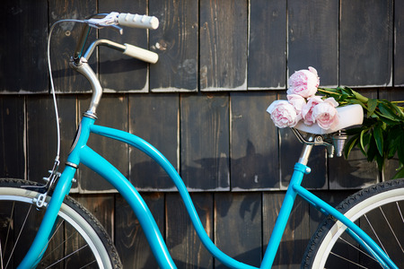 Close-up of a blue vintage bicycle on which lies a bouquet of gently pink peonies on a dark wall background.の写真素材