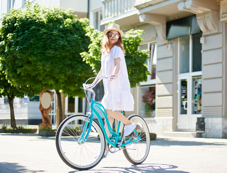 Full length portrait of a happy young long haired woman wering a dress sunglasses and a hat enjoyfing cycling in the city copyspace nature happiness emotions cyclist.の写真素材