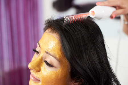 Closeup of hair treatment procedure performed to a brunette client of a beauty salon who has a gold mask on her face.の写真素材