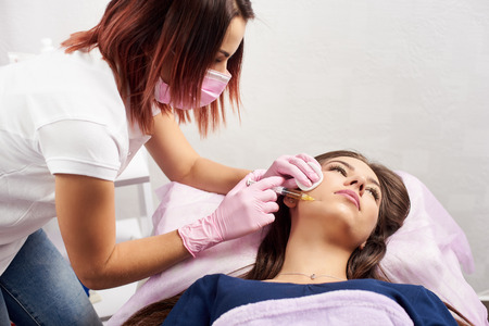 Woman getting injection in the cosmetology salon. Doctor in medical gloves and mask with syringe...