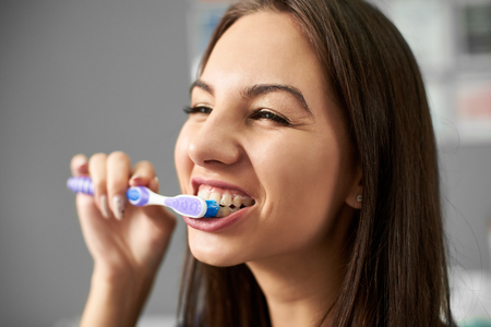 Young attractive brunette is cleaning her teeth with a toothbrush and smiling and being happy about this.の写真素材