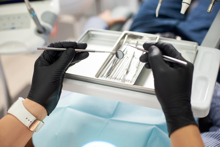 Macro photo of a dentist in a black glove takes a tool to treat the patient. The concept of modern dentistryの写真素材
