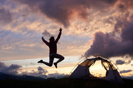 Female tourist jumping high adoring beautiful scenery around on moutain hill in Romania. Girl woman climber tent night clouds magnificent breathtaking beautiful view nature landscapeの写真素材