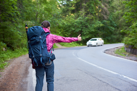 Rearview shot of a female traveller with a backpack cathicng a car on the Bicaz Canyon road copyspace travelling tourism backpacking transport transportation lifestyle active exploring.の写真素材