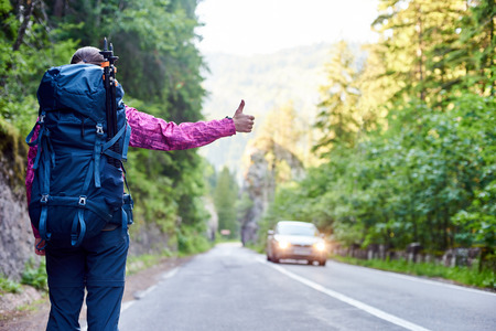 Traveler woman with backpack is catching a car on road in the Bicaz Gorge in Cheile Bicazului-Hasmas National Park Romaniaの写真素材