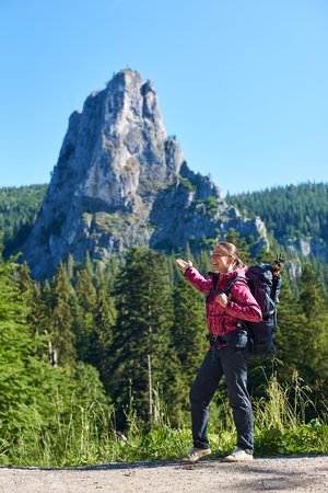 Happy tourist female with a backpack in Cheile Bicazului-Hasmas National Park Romania. A beautiful landscape of mountains, forests and blue sky above them on a sunny dayの写真素材