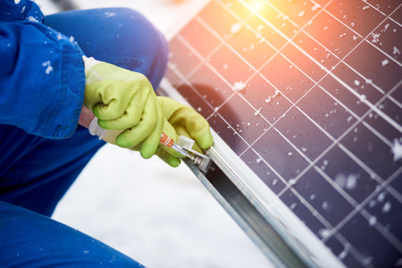 Cropped close up of a professional electrician in protective uniform and gloves installing solar...