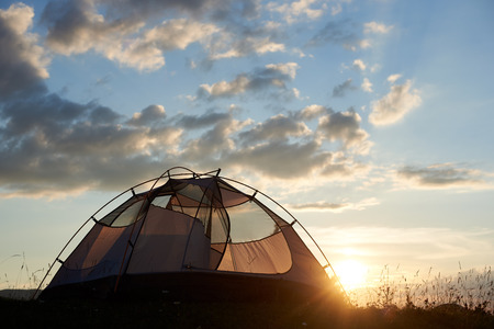 The tent stands on top of a mountain at sunset under the sky with rare clouds and evening sun on a blurred background. The concept of healthy recreation in the mountainsの写真素材