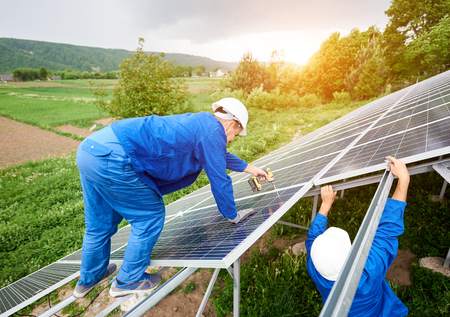 Construction worker connects photo voltaic panel to solar system using screwdriver. Professional installing and construction of solar system, alternative energy and financial investment concept.の写真素材