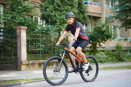 Athletic guy biker in cycling clothes and helmet looking to camera riding bicycle near beautiful buildings. Man training, improving hobby, getting ready for contestの写真素材