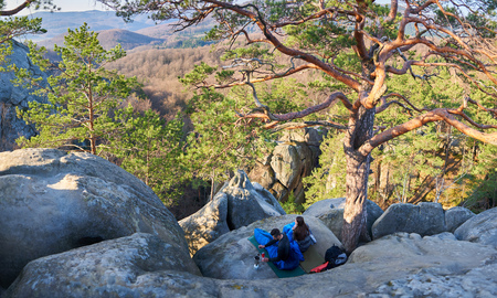 View from above of young tourist couple in mountains, handsome man and pretty girl sitting in sleeping bags and having coffee on big rocks enjoying peaceful morning. Tourism and traveling concept.の写真素材