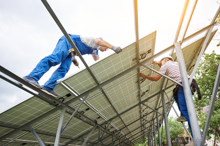 Stand-alone solar photo voltaic panel system installing. View from below of three technicians workers mounting heavy solar panel. Alternative energy production and professional construction concept.の写真素材