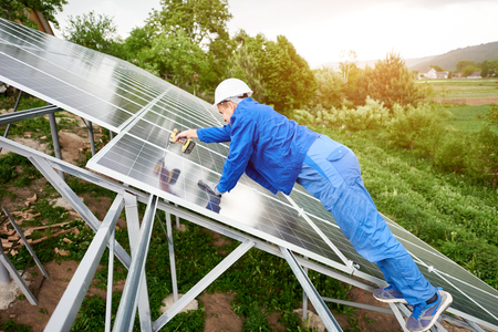Construction worker connects photo voltaic panel to solar system using screwdriver. Professional installing and construction of solar system, alternative energy and financial investment concept.の写真素材