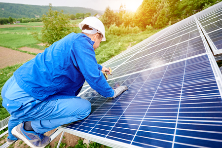 Construction worker connects photo voltaic panel to solar system using screwdriver. Professional installing and construction of solar system, alternative energy and financial investment concept.の写真素材