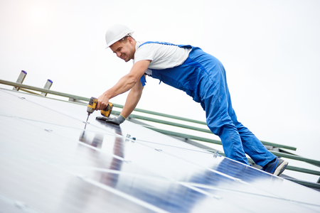 Construction worker connects photo voltaic panel to solar system using screwdriver. Professional installing and construction of solar system, alternative energy and financial investment concept.の写真素材