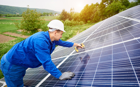 Construction worker connects photo voltaic panel to solar system using screwdriver. Professional installing and construction of solar system, alternative energy and financial investment concept.の写真素材