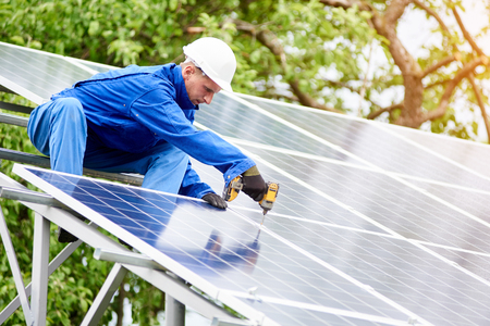 Young construction worker connects photo voltaic panel to solar system using screwdriver on bright sunny day. Alternative cheap sun energy production and profitable financial investment concept.の写真素材