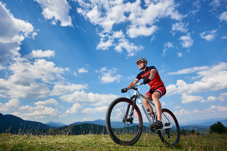 Athletic professional sportsman cyclist in sportswear and helmet cycling cross country bike in Carpathian mountains against blue sky with clouds on summer. Active lifestyle and outdoor sport conceptの写真素材