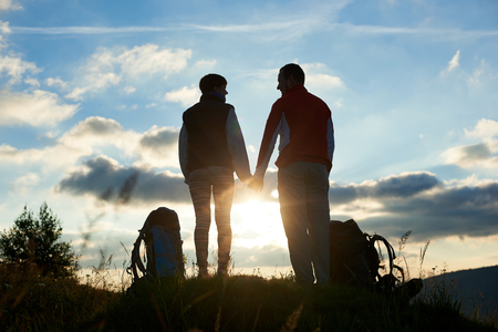 Silhouettes of a man and a woman looking at each other and holding hands against the backdrop of a bright sunset in the mountains, bottom viewの写真素材