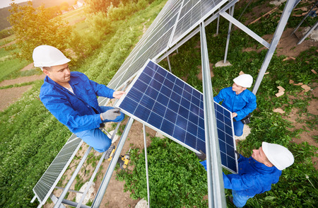 Team of three technicians mounting photo voltaic panel to stand-alone solar system platform on bright sunny day. Alternative energy, professionally done job and financial investment concept.の写真素材