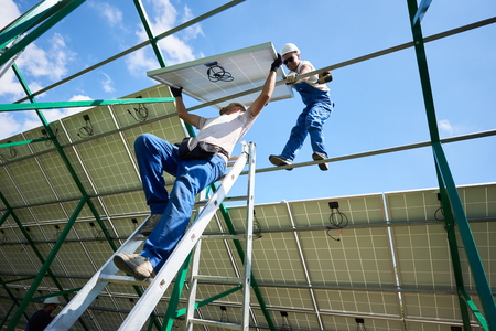 Workers mounting solar batteries on metallic construction. risky work for professionals. Modern solution for natural resources saving, using renewable solar energy. Environment friendly, green energy.の写真素材
