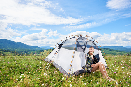 Young happy woman hiker hiking mountain trail, sitting inside tent, enjoying summer sunny morning in Carpathian mountains. Camping concept adventure vacations outdoorの写真素材