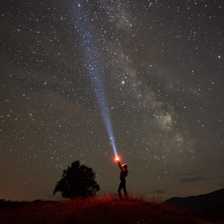 Silhouette of woman standing against night starry sky with Milky Way in the mountains with a...