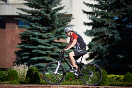 Male cyclist in professional cycling clothing and helmet training on street edge, ready to jump. Man exercising before contest, improving riding skills. Concept of motivation, achievement, successの写真素材
