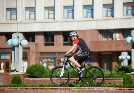 Young man biker in professional cycling clothing and helmet training on street edge, ready to jump. Man exercising before contest, improving riding skills. Concept of motivation, achievement, successの写真素材