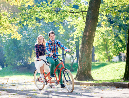 A young active couple, bearded man and long-haired blond woman riding a tandem bicycle.の写真素材