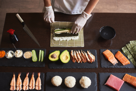Master making a sushi roll with nori, rice, cucumber and omelet using bamboo mat. Closeup view of process. View from the topの写真素材