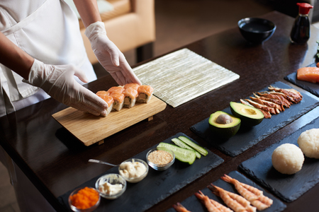 Close-up view of process of preparing rolling sushi. Chef is serving fresh delicious rolls on the wooden board.の写真素材