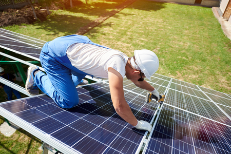 Professional worker installing solar panels on the green metal construction, using different equipment, wearing helmet. Innovative solution for energy solving. Use renewable resources. Green energy.の写真素材