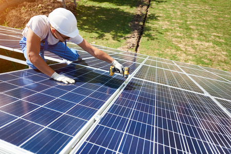 Professional worker installing solar panels on the green metal construction, using different equipment, wearing helmet. Innovative solution for energy solving. Use renewable resources. Green energy.の写真素材