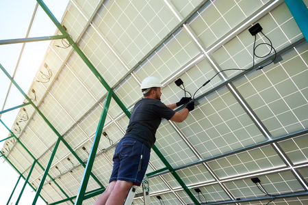 Professional worker installing solar panels on the green metal construction, using different equipment, wearing helmet. Innovative solution for energy solving. Use renewable resources. Green energy.の写真素材
