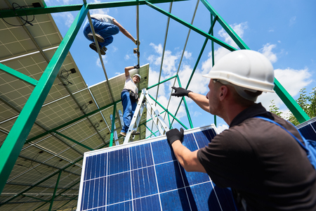 Professional workers team installing solar panels on the green metal construction using different equipment. Innovative solution for energy solving. Use renewable resources. Green energy.の写真素材