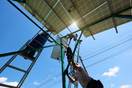 Professional workers team installing solar panels on the green metal construction using different equipment. Innovative solution for energy solving. Use renewable resources. Green energy.の写真素材