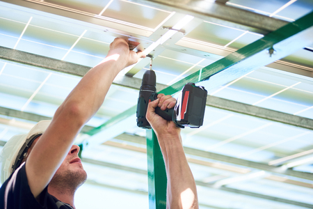 Worker using drill by solar panels installing. Innovative high-tech exterior. Modern solution for natural resources saving, using renewable solar energy. Environment friendly. New technologies.の写真素材