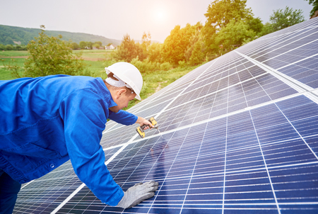 Construction worker connects voltaic panel to solar system using screwdriver. Professional installing and construction of solar system, alternative energy and financial investment concept.の写真素材