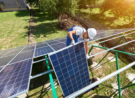 Professional workers team installing solar panels on the green metal construction using different equipment. Innovative solution for energy solving. Use renewable resources. Green energy.の写真素材