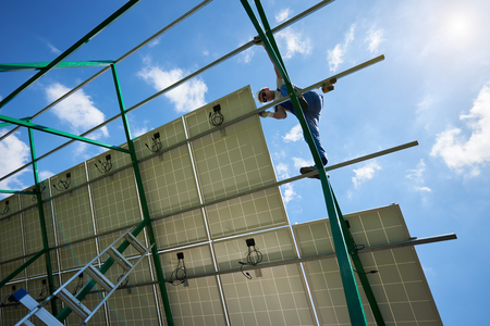 Professional worker installing solar panels on metallic carcass. Solar batteries mounted on green metallic construction. Modern solution for natural resources saving, using renewable solar energy.の写真素材