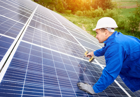 Construction worker connects photo voltaic panel to solar system using screwdriver. Professional installing and construction of solar system, alternative energy and financial investment concept.の写真素材