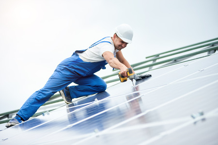 Construction worker connects photo voltaic panel to solar system using screwdriver. Professional installing and construction of solar system, alternative energy and financial investment concept.の写真素材
