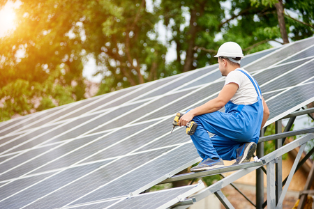 Construction worker with screwdriver connecting photo voltaic panels on solar system shiny surface background. Alternative energy, ecology protection and cheap electricity production concept.の写真素材