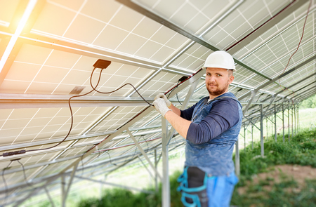 Installing and wiring of stand-alone solar photo voltaic panel system. Close-up of young electrician in hard-hat connecting electrical cables inside the solar modules. Alternative energy concept.の写真素材