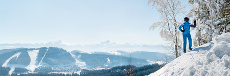 Panoramic shot of a female skier resting on top of the mountain observing nature at ski resort on a beautiful sunny winter day copyspace peaceful recreational vacation travel conceptの写真素材