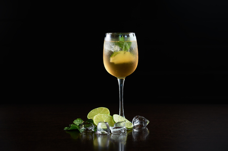 Tall elegant crystal cocktail glass with cold summer refreshing juicy drink, thin slices of lime, fresh green mint leaves and transparent ice cubes isolated on deep black copy space background.の写真素材